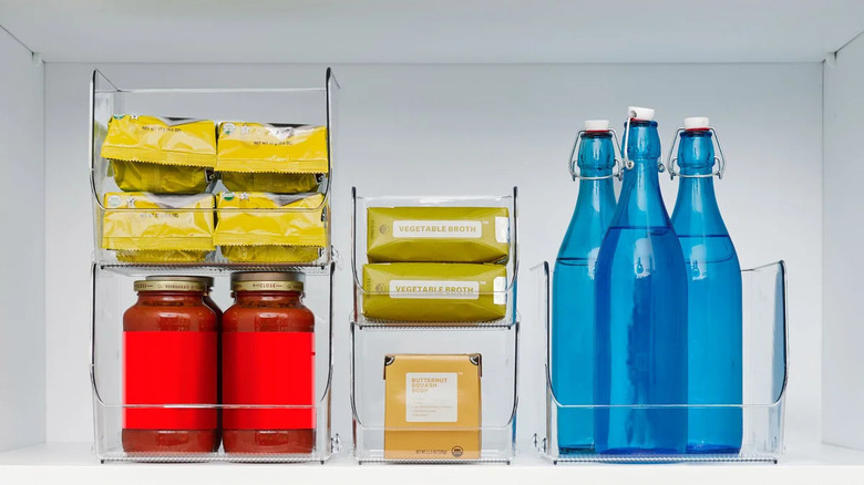 Transparent bins stacked on a white shelf and contain jars, bottles, and packages