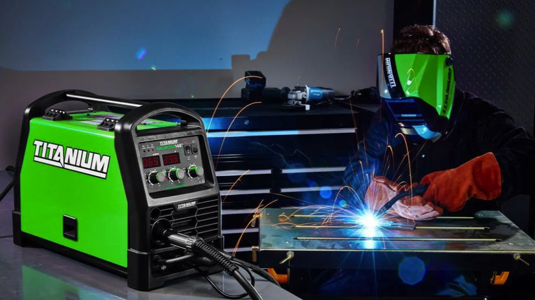 Titanium welder sitting on a shop table near a man welding in a garage
