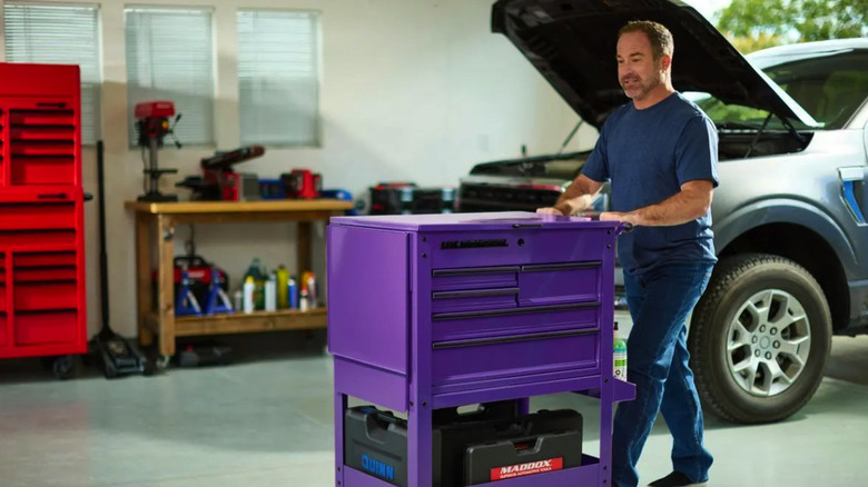 Man pushing a 30-inch 5-drawer mechanics drawer across a garage near a truck with an open hood