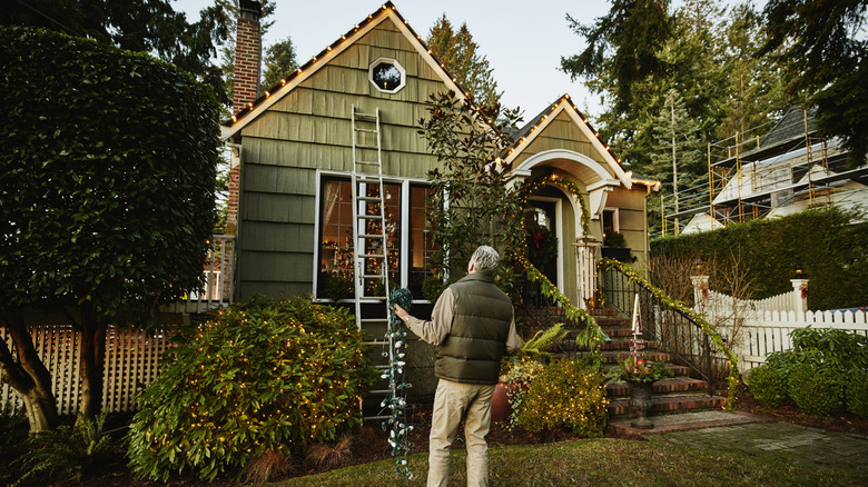 A man putting lights on a green house with a brown roof.