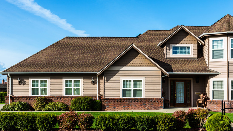 A beige house with a brown roof and a groomed yard with bushes.