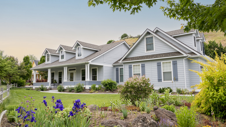 A soft grey house with blue shutters and a light brown roof.