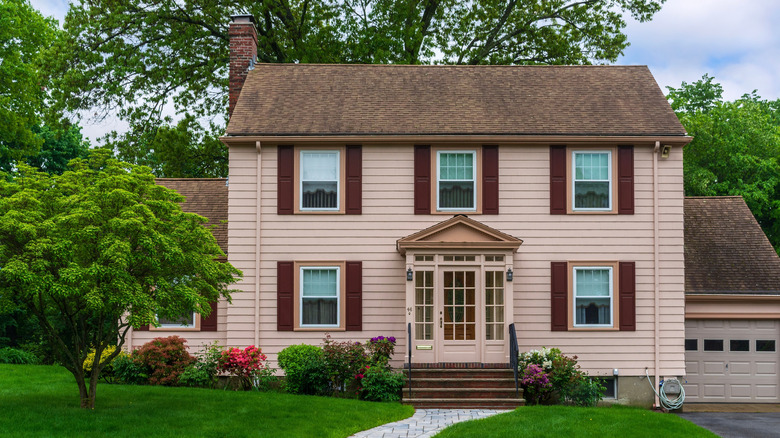 A pink house with a brown roof and lush green yard.