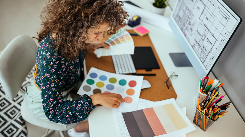 Woman looking at a color swatch while a room's blueprint is open on her PC