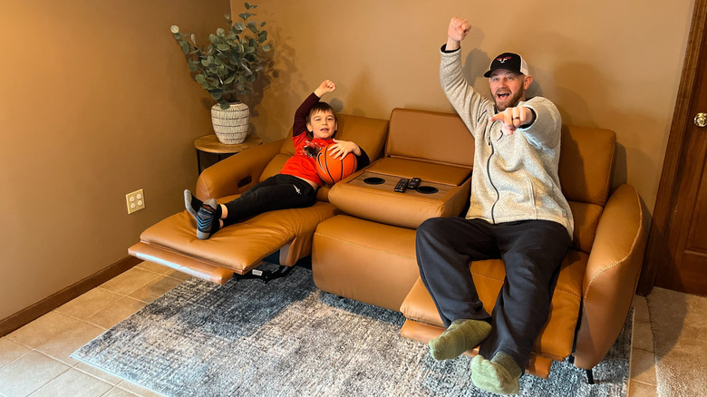 A man and young boy cheer while sitting on a leather recliner sofa