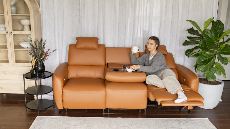 A young woman stretches out on a leather sofa