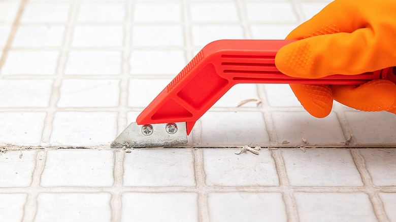 Gloved hand removing tile grout