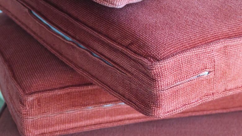 A stack of red-orange colored couch cushions with the zippers showing.