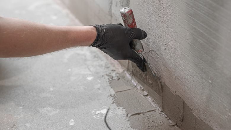 Gloved hand applying drywall to corner with putty knife
