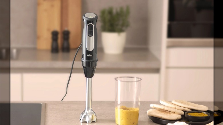 The Braun MultiQuick 5 Pro 4-in-1 Immersion Blender next to a jar of hummus and some pita bread on a countertop in a kitchen.