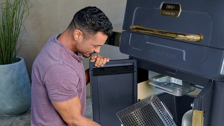 A man takes the accessories out of the inside of a Ninja FlexFlame Outdoor Cooking System in a patio.