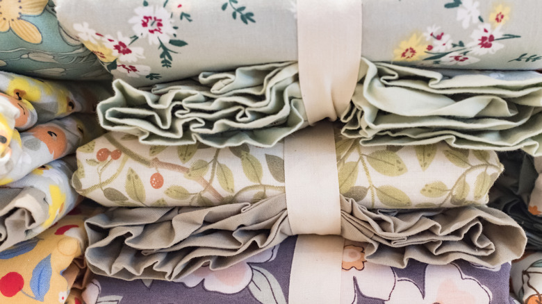 A close up of bundled bed sheets on a shelf in various colors and patterns