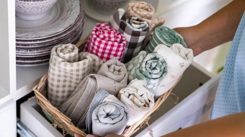 A series of cloth napkins in all various colors and patterns rolled up and placed into a basket