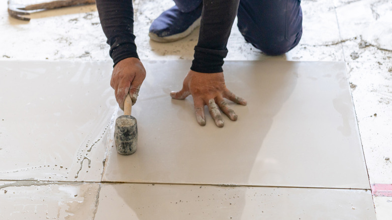 A person uses a dirty rubber mallet with a black head and wooden handle to install flooring
