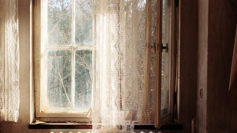 Vintage white lace floral curtains covering an old window