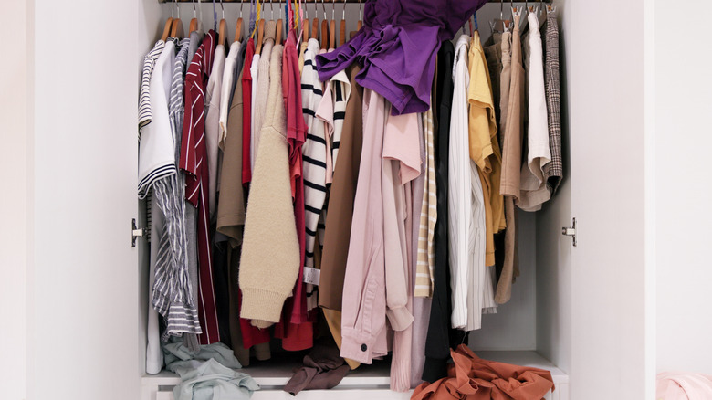 small closet with clothes hanging messily and no organization