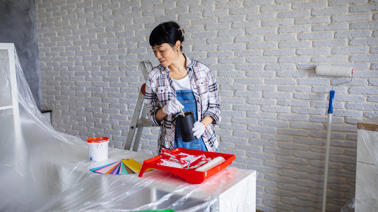 A woman looking at a colorful paint swatch kit while mixing paints in a covered room