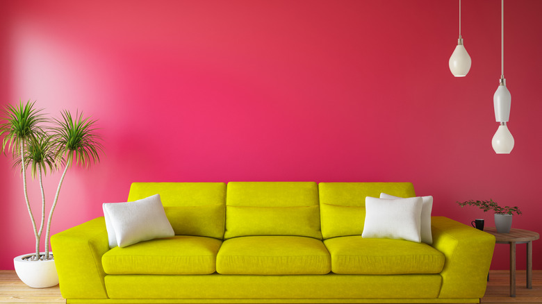 A pink wall with a bright yellow couch