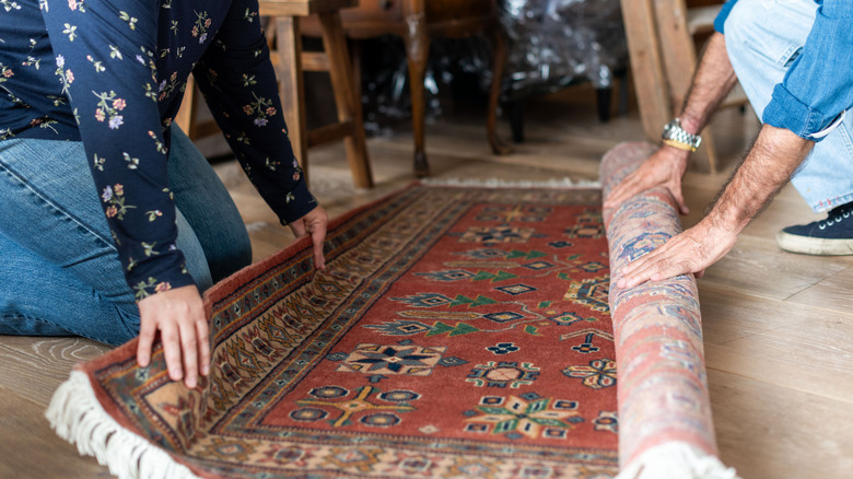 Two people crouched on the ground unraveling a Persian rug.