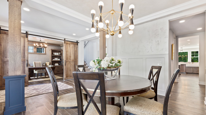 Open concept dining room area with round table with six chairs and a pendant light, and barn doors open to an office area