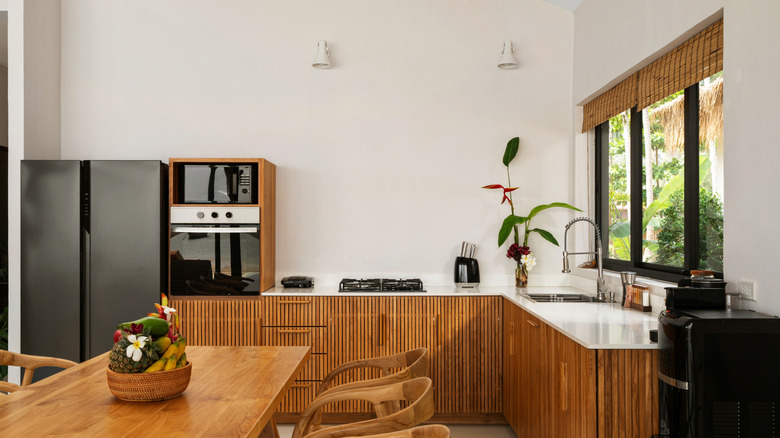 A bright kitchen with wooden cabinets, bamboo roller blinds, and a dining table in a modern luxury villa.