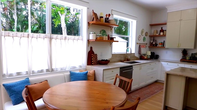 Beautifully decorated kitchen with white cabinets, warm wood table, and cafe curtains covering bottom half of windows.