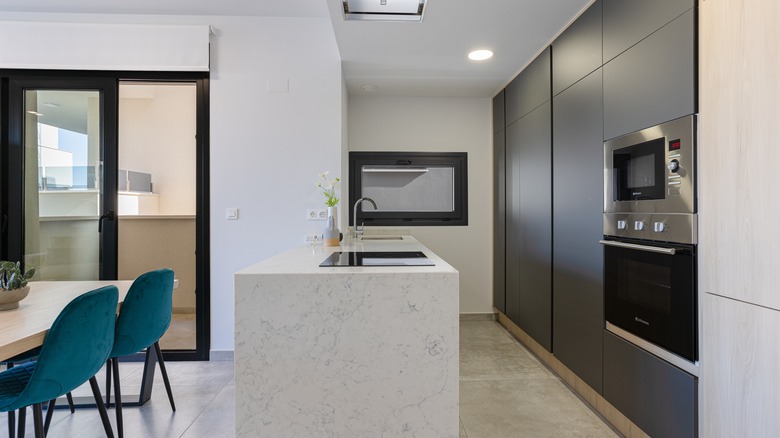 Modern kitchen design featuring blackout shades, sleek cabinets, marble island, built-in oven, and minimalist layout.