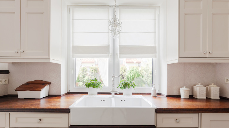 Elegant kitchen with white cabinets, dark wood countertop, white porcelain sink, and white window shades.