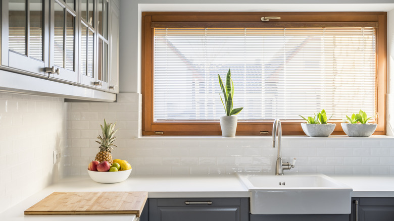 Light kitchen with white countertop, sink, Venetian blinds, and grey furniture