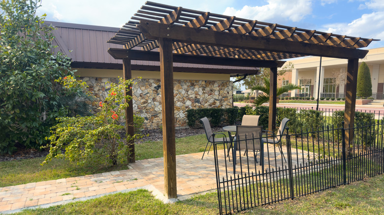 A pergola with a paved floor and seating around a small table.