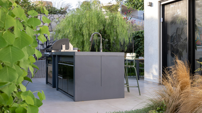A metal bar cabinet contains a grill station and a sink on a patio.