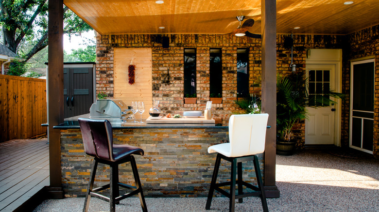 A stone outdoor bar cabinet has two bar stools facing towards it.