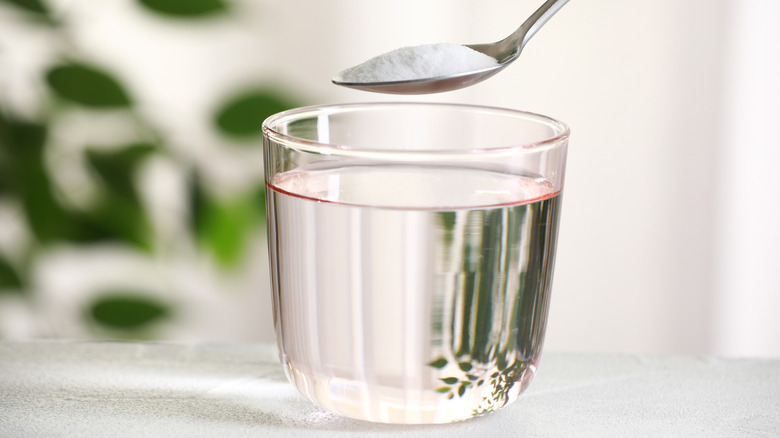 A spoon containing baking soda to be poured in glass of water