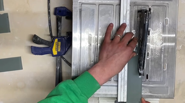Hands cutting a corner off a glass tile with a wet saw