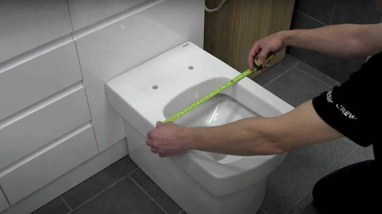 Someone measuring toilet seat