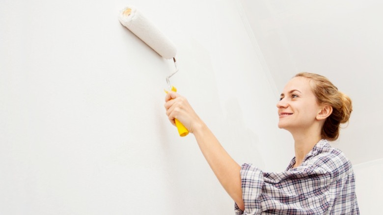 Woman rolling white primer onto a clean interior wall