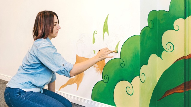 Person painting a mural over prepared interior house wall
