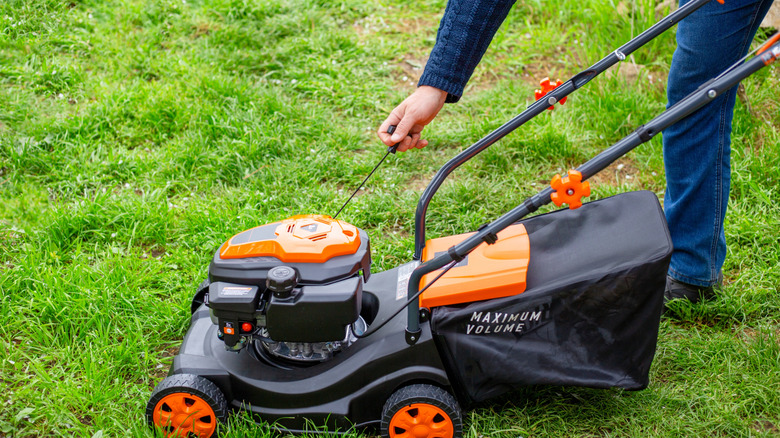 Hand pulling the starter cord of a lawn mower