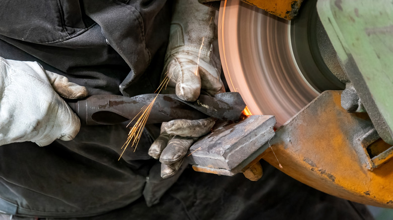 Person with gloved hands sharpening a drill bit using a bench grinder