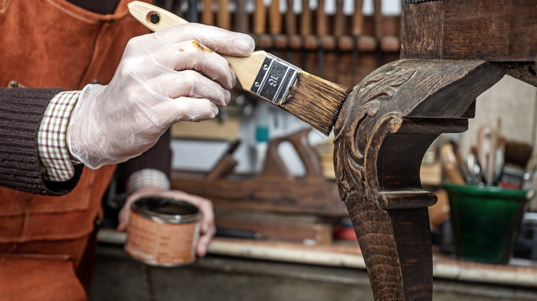 Hands staining the leg of an antique wood furniture