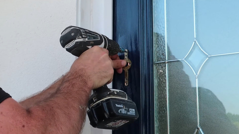 A man mounting a door knocker plate into the door with a drill.