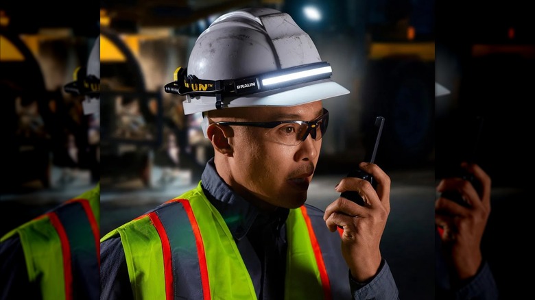 person wearing BRAUN headlamp over hard hat while using walkie talkie radio