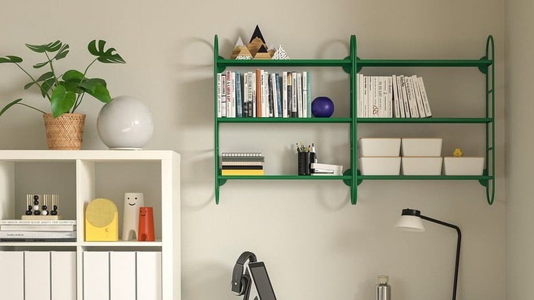 An IKEA green wall shelf mounted to the wall holds books, stationery, and knicknacks.