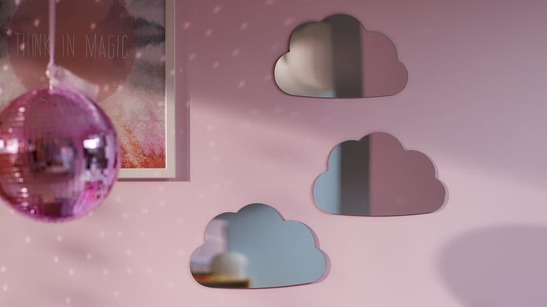 Cloud-shaped mirrors are displayed on a pink wall next to a framed photo and a pink disco ball.