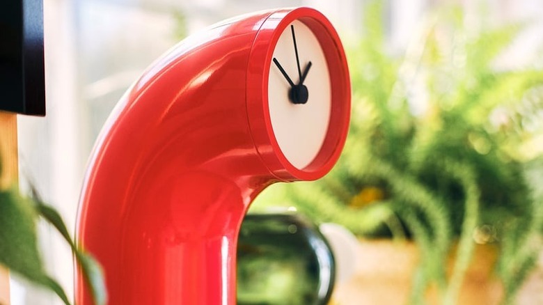 A photo features a red tube-shaped clock against a blurred home interior background.