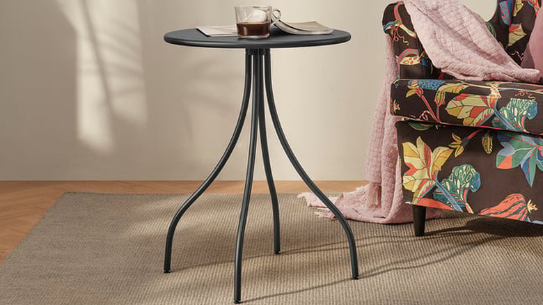An IKEA side table holds a vase and drink, placed next to a sofa.