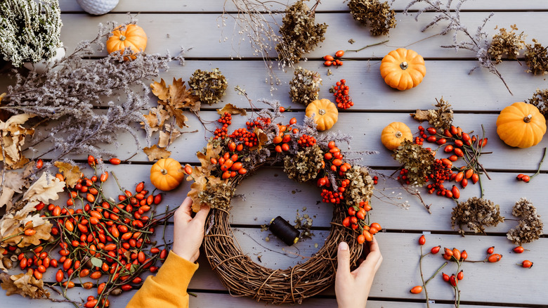 A person creating a willow wreath decorated with leaves, stems, and rose hips