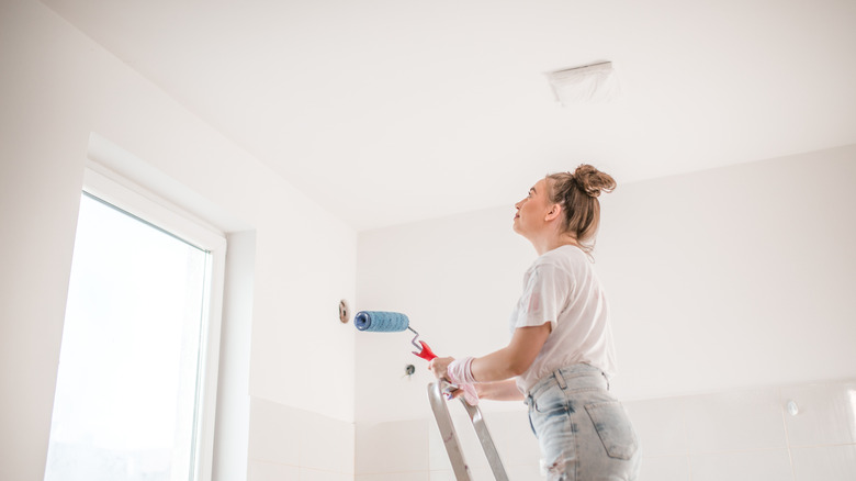 A woman standing on a ladder preparing to paint the ceiling