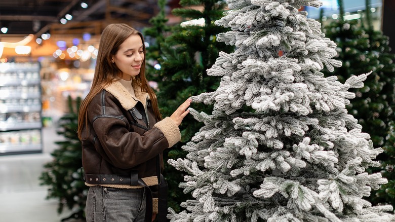 a young woman selects an artificial christmas tree