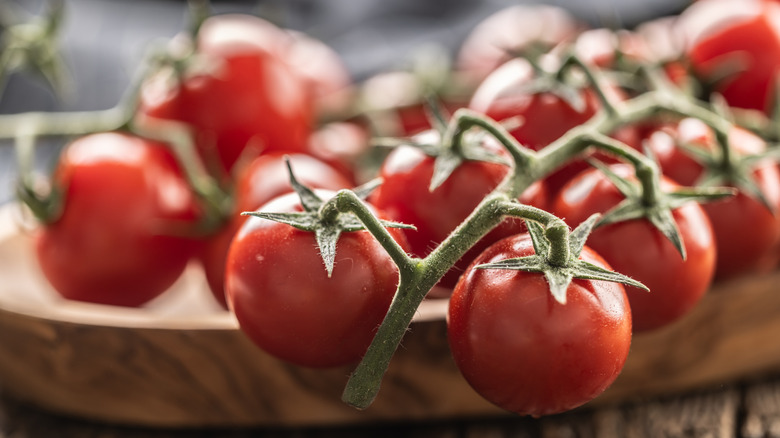 Cluster of red cherry tomatoes on the vine resting on a wooden cutting board.